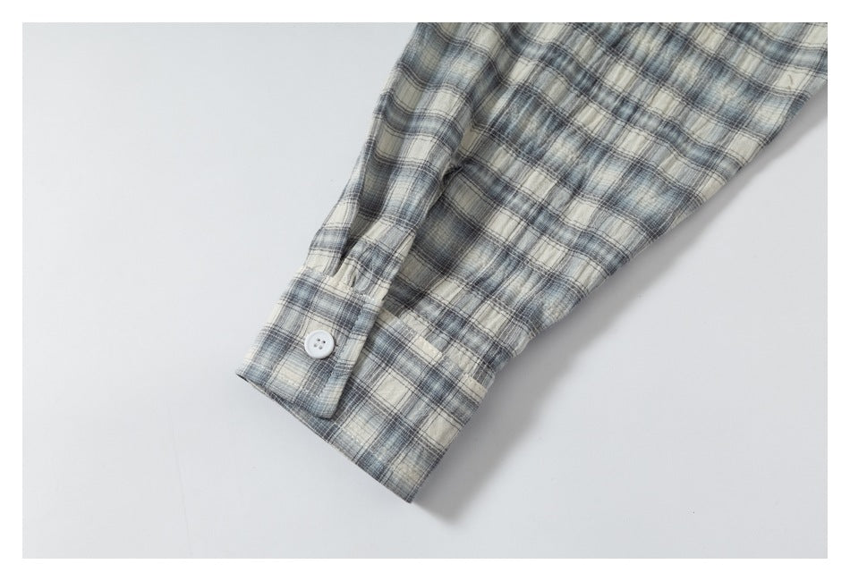 Close view of a buttoned cuff and sleeve in gray, blue, and cream plaid.