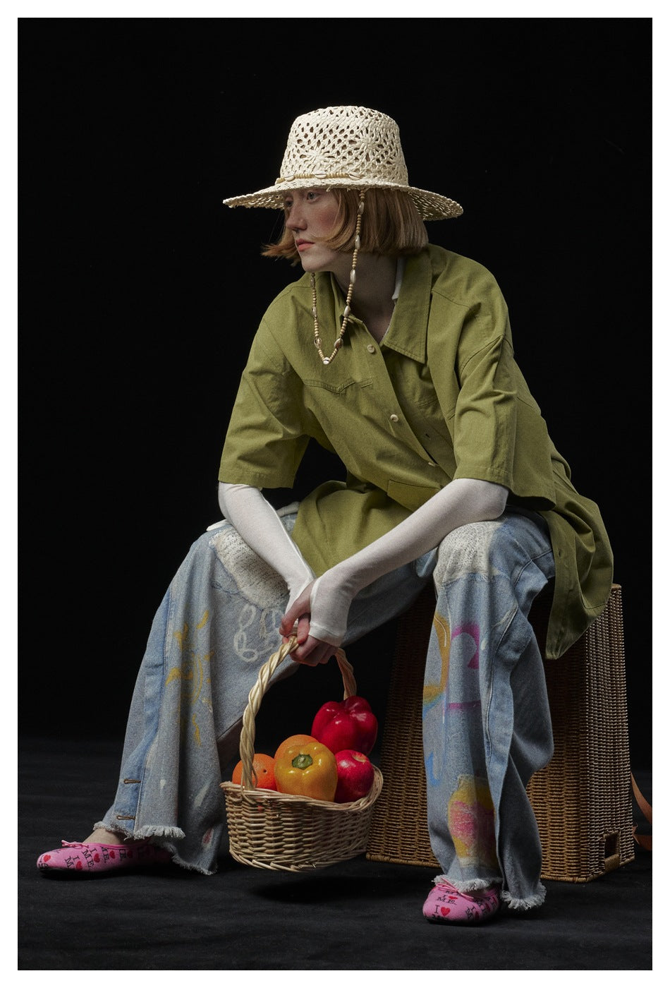 Model wearing an oversized olive-green short-sleeve button-up shirt with jeans and a woven hat.