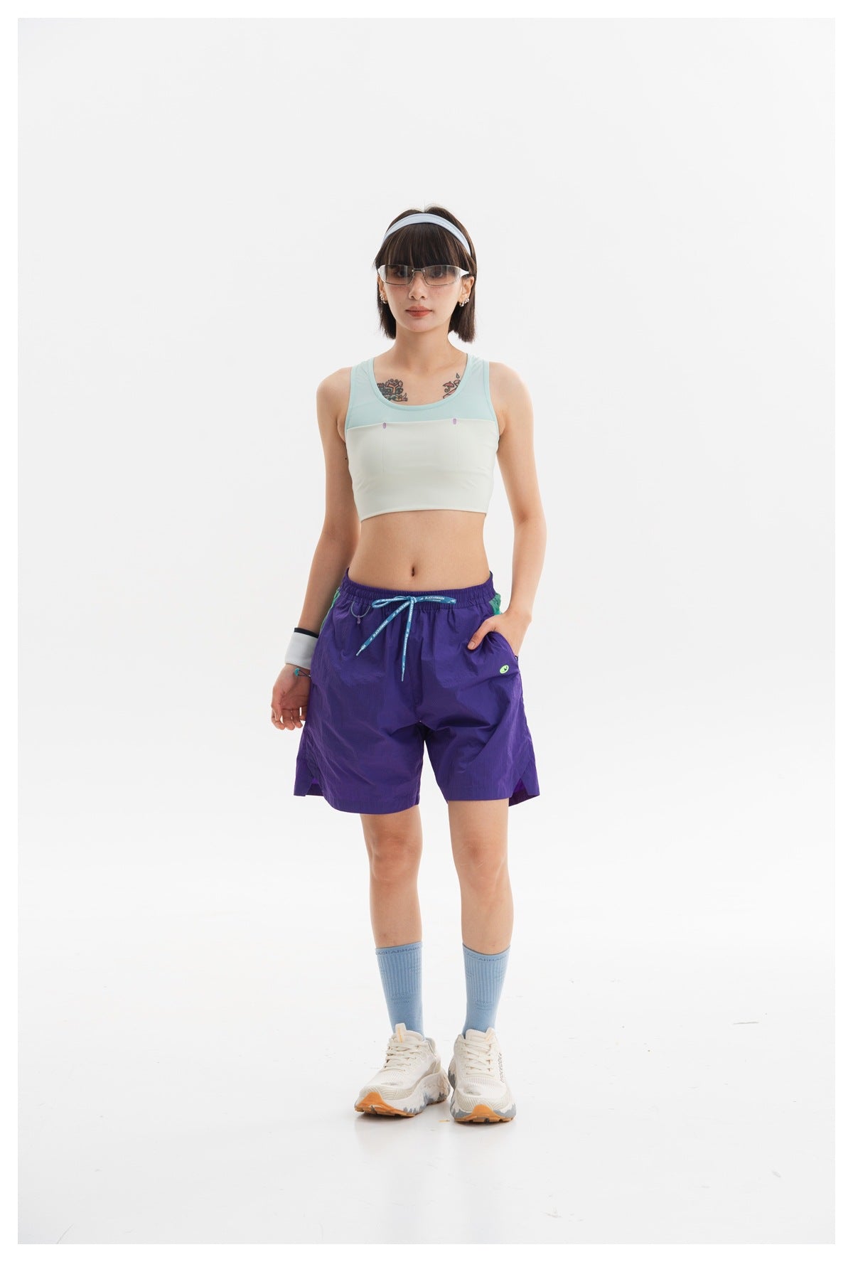 Full-length model wearing a mint and ivory cropped tank, purple shorts, blue socks, and white sneakers.