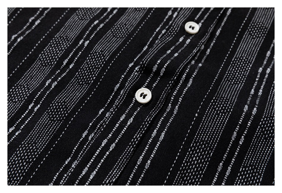 Close-up of black fabric with irregular white dashed stripes and two white buttons along the placket.