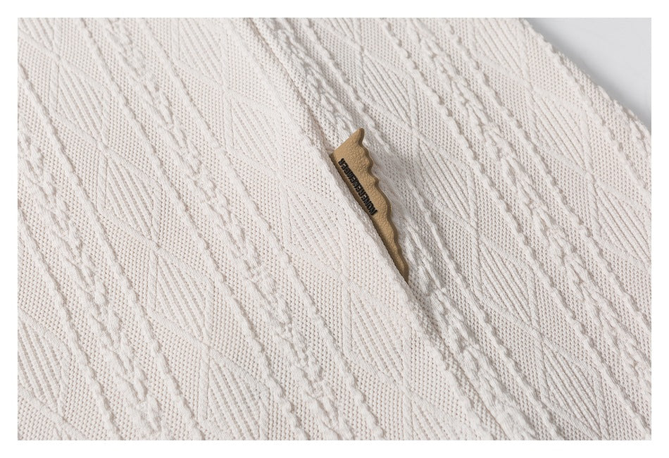 Close-up of off-white cable-pattern knit fabric with a small tan label bearing dark lettering.