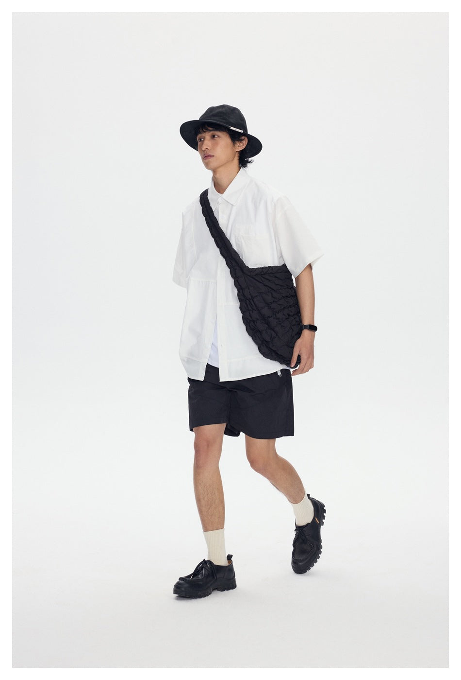 Model wearing a white short-sleeve shirt, black shorts, and a textured black crossbody bag.