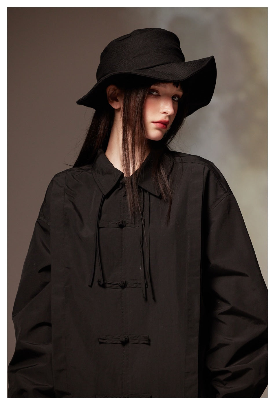 Close-up of a model in a black wide-brim hat and black frog-closure jacket.