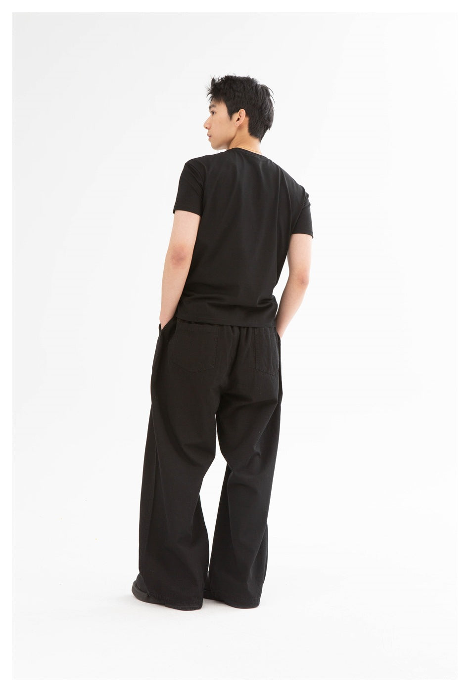 Back view of a model wearing a plain black T-shirt and loose black trousers.