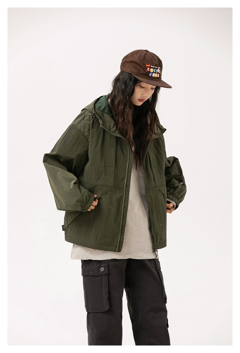 Model wearing an olive-green hooded zip jacket with front pockets and a brown cap.