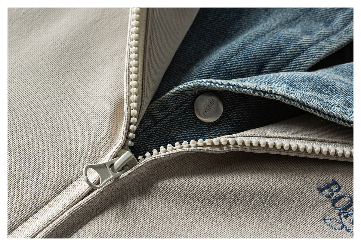 Close-up of a white zipper, blue denim panel, and partial dark embroidery on a taupe garment.