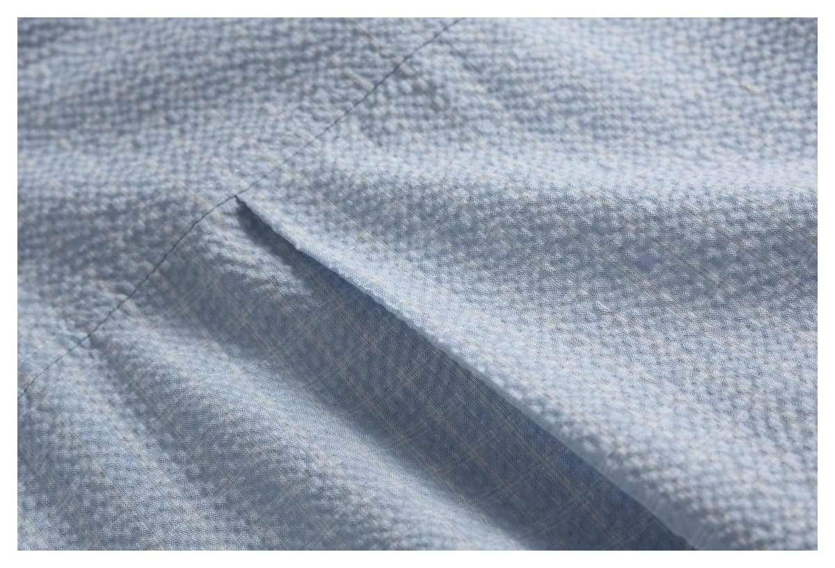 Close-up of a diagonal seam and folded fabric in light blue-gray textured material.