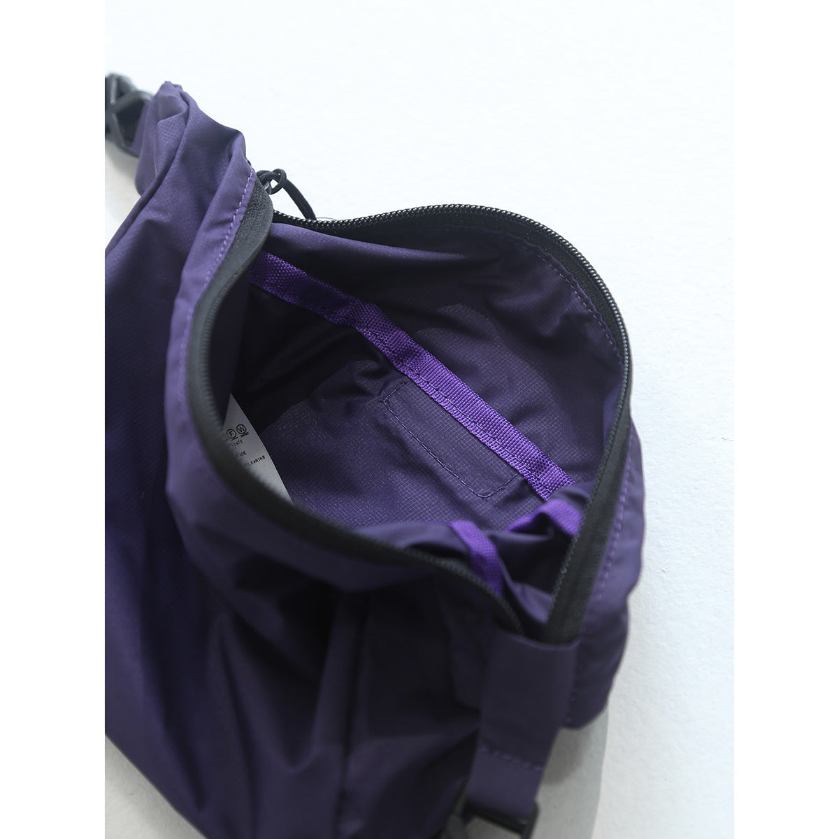 Close-up of an open purple bag showing its zippered opening, dark lining, and interior pocket.