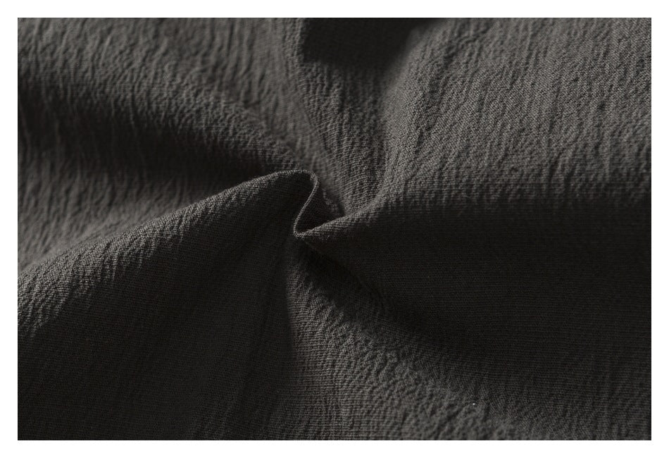 Macro view of dark charcoal garment fabric gathered into a fold, showing its textured surface.