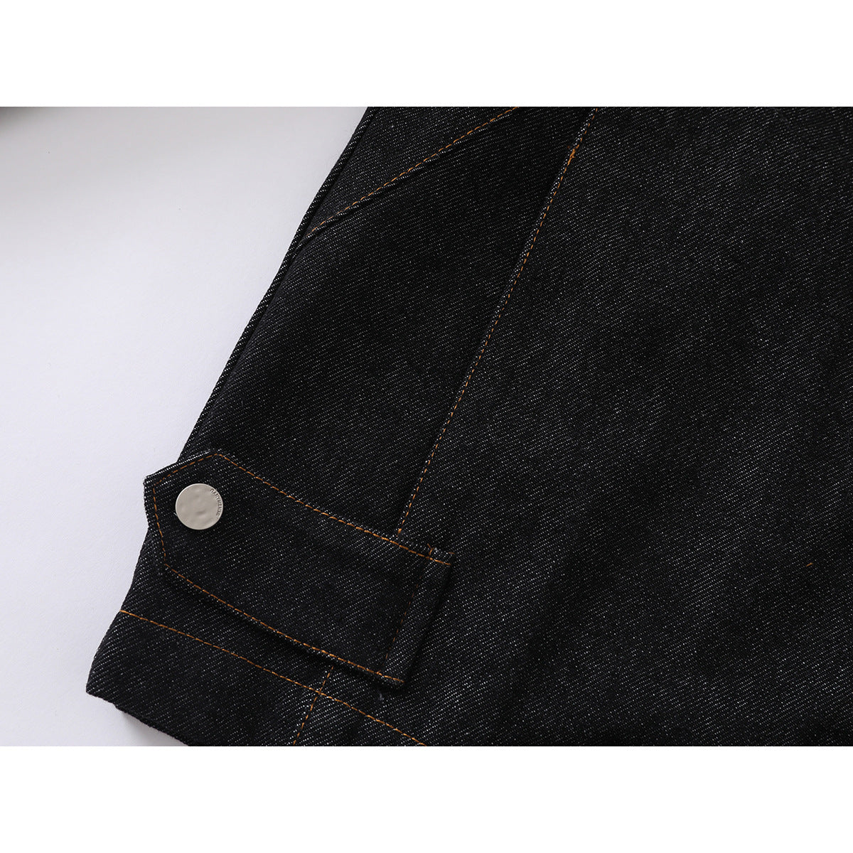 Close-up of a black denim jacket sleeve cuff with a silver snap and contrasting stitched seams.