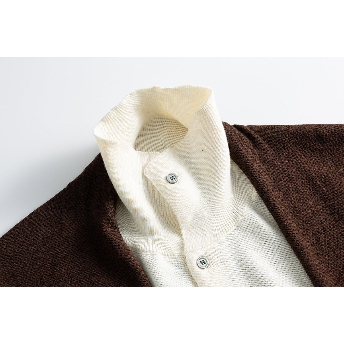 Close-up of an ivory high collar and button placket beneath a dark brown knit cardigan.