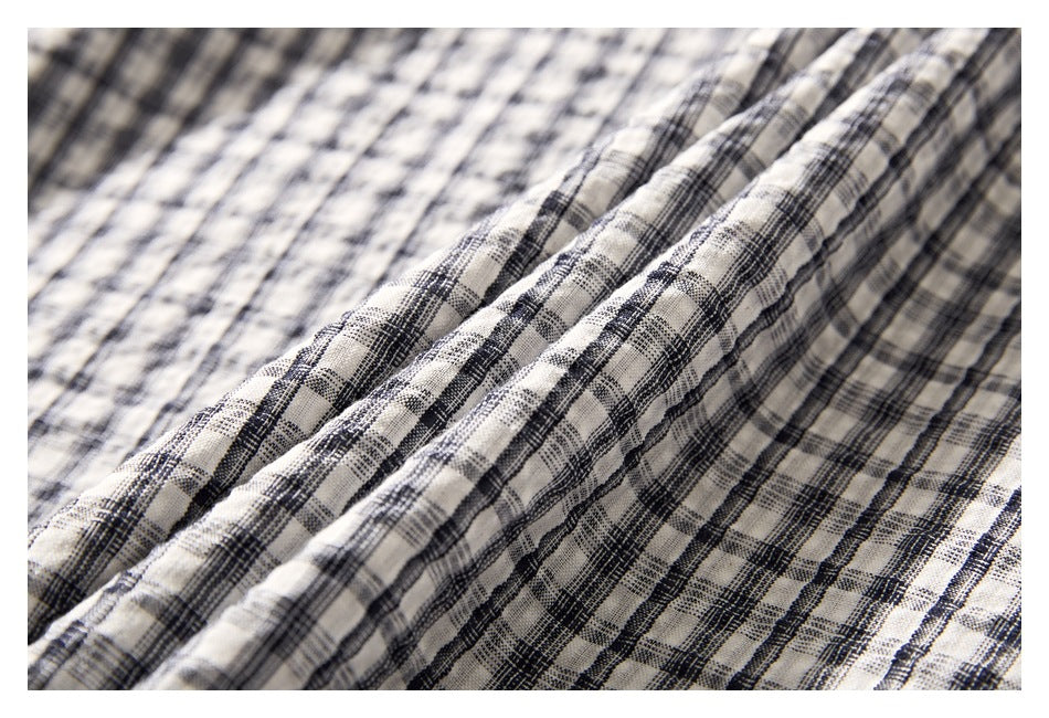 Close-up of cream fabric with a black and gray plaid pattern and softly gathered folds.