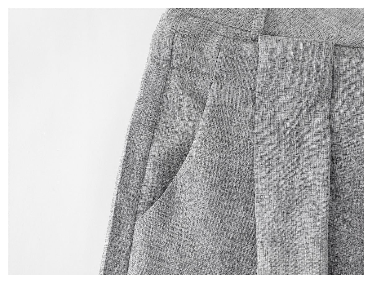 Close-up of light gray textured trousers showing a slanted pocket and front pleat.