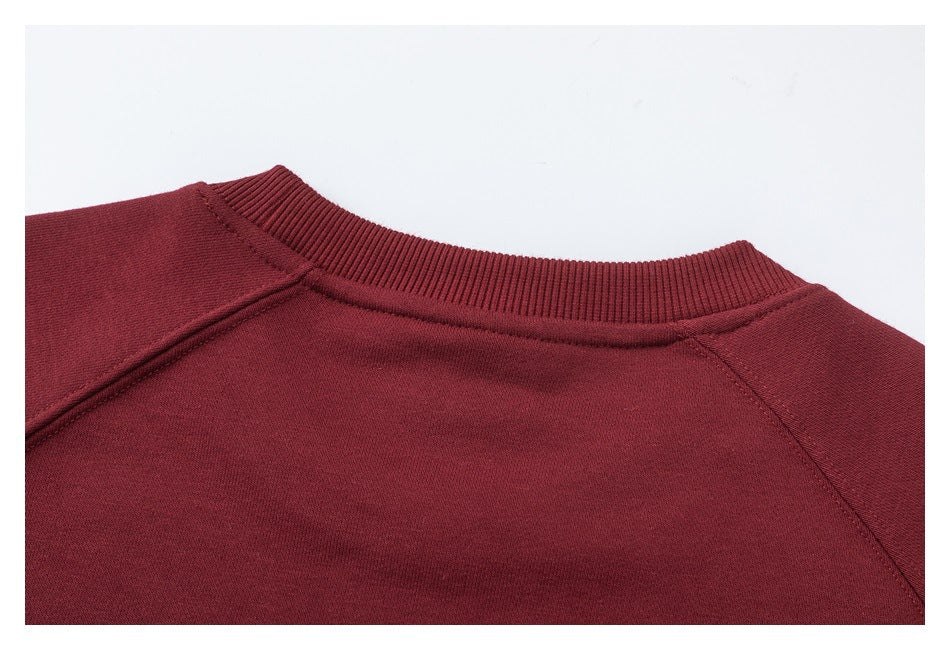 Close-up of a burgundy sweatshirt's ribbed crew neckline and raglan shoulder seams.