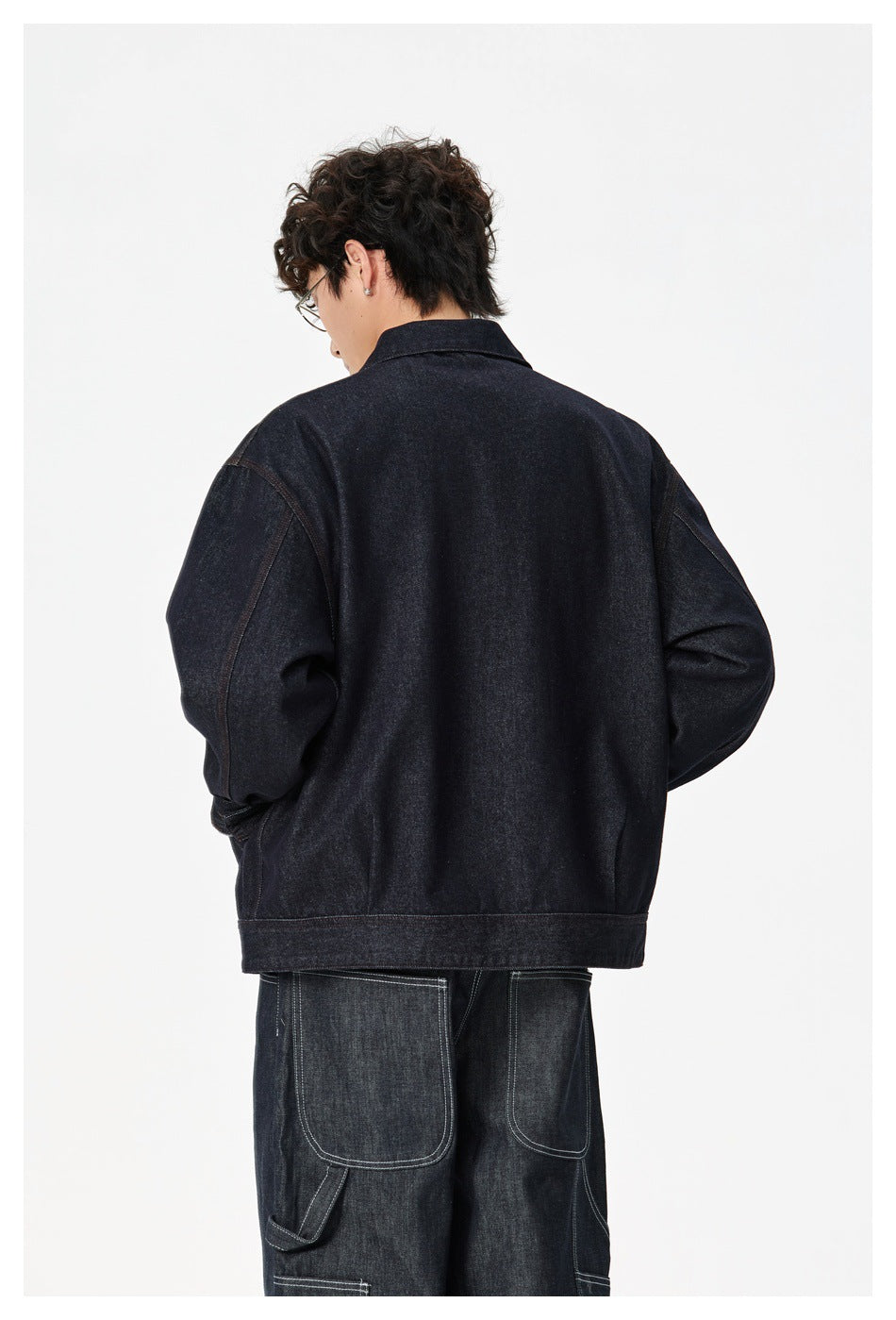 Back view of a model wearing a dark indigo denim jacket with a broad hem and relaxed sleeves.
