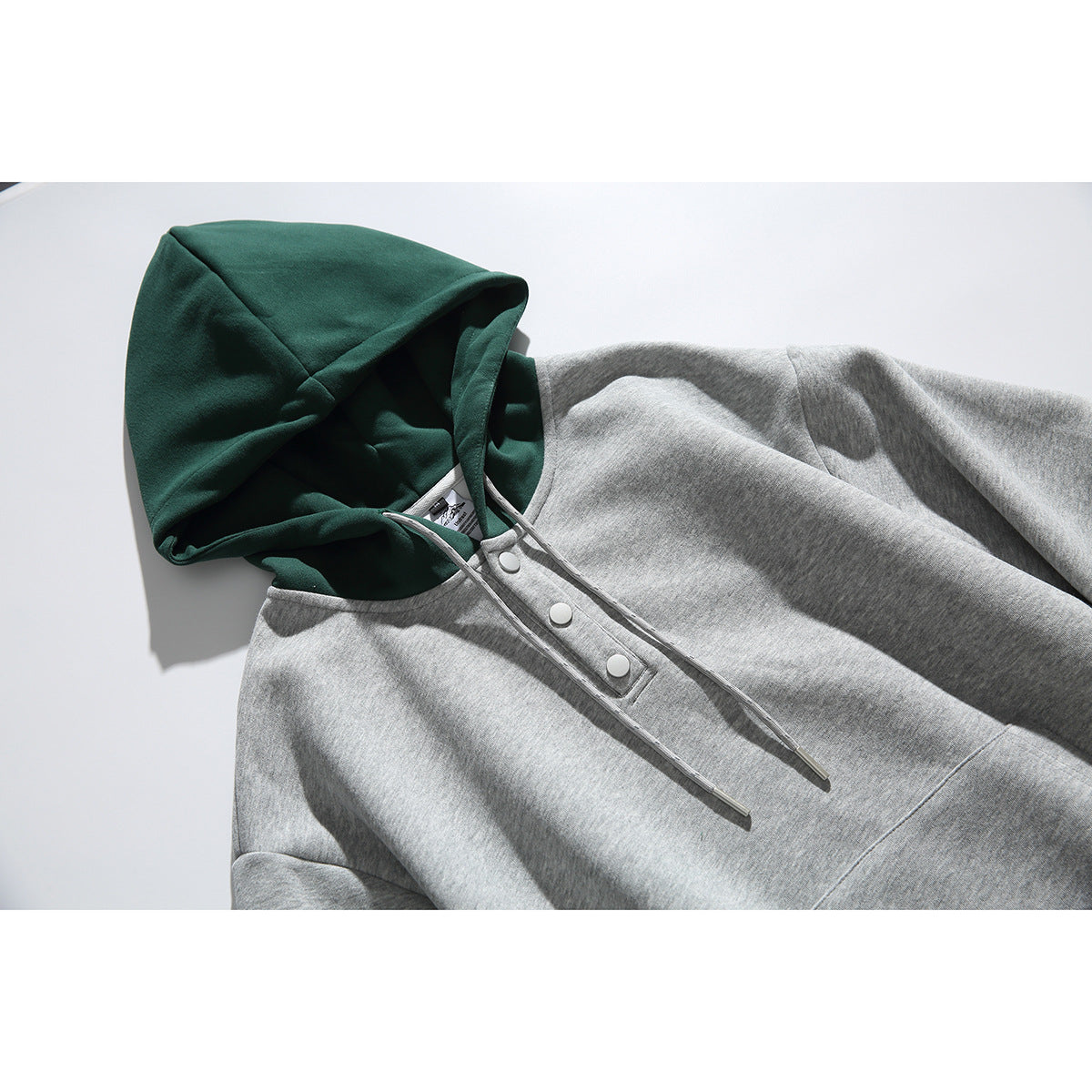 Close-up of a gray hoodie with a dark green hood, drawstrings, and a three-button placket.