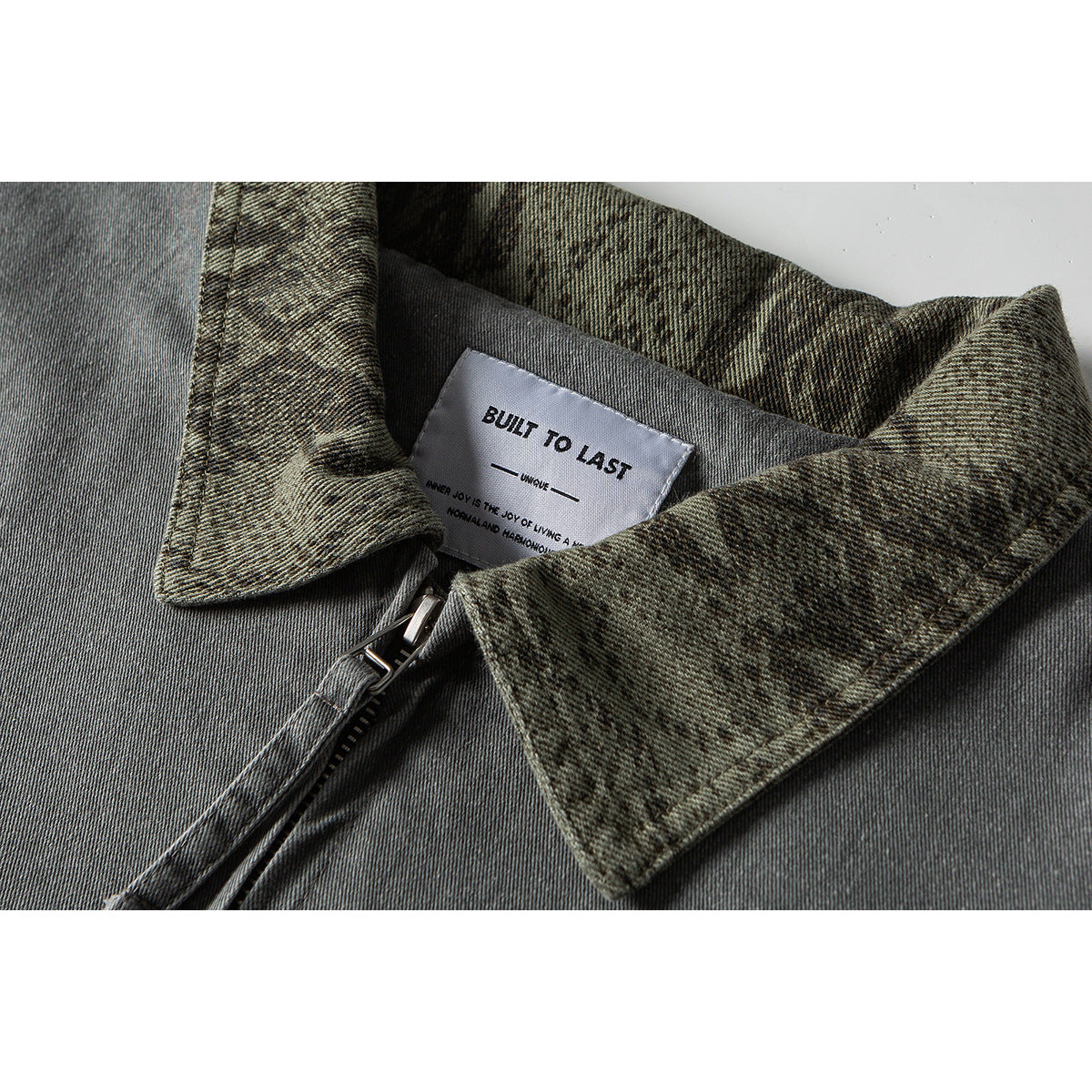 Close-up of a gray jacket collar with mottled olive lining, a front zipper, and a sewn-in label.