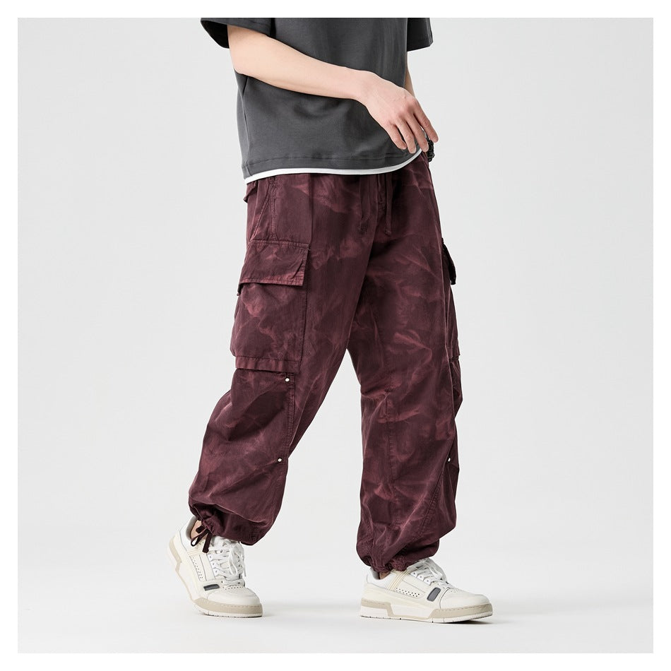 Angled view of a model wearing loose burgundy cargo pants with large cargo pockets and gathered ankle cuffs.