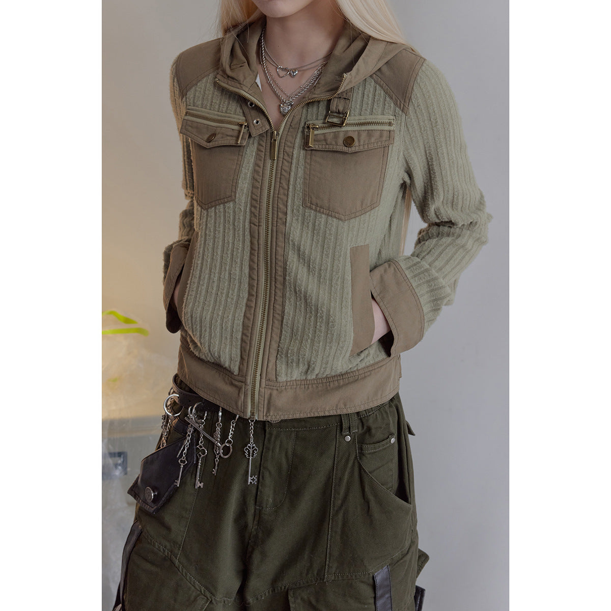 Close view of a model wearing a sage ribbed zip jacket with tan panels, chest pockets, and a hood.