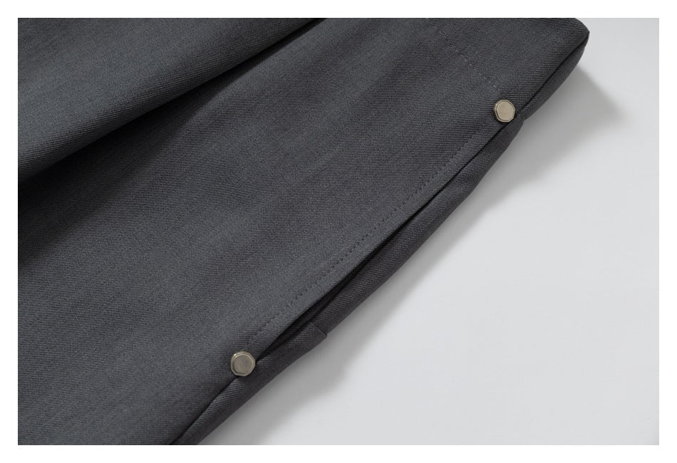 Close view of a trouser edge with two small metal buttons on dark charcoal fabric.