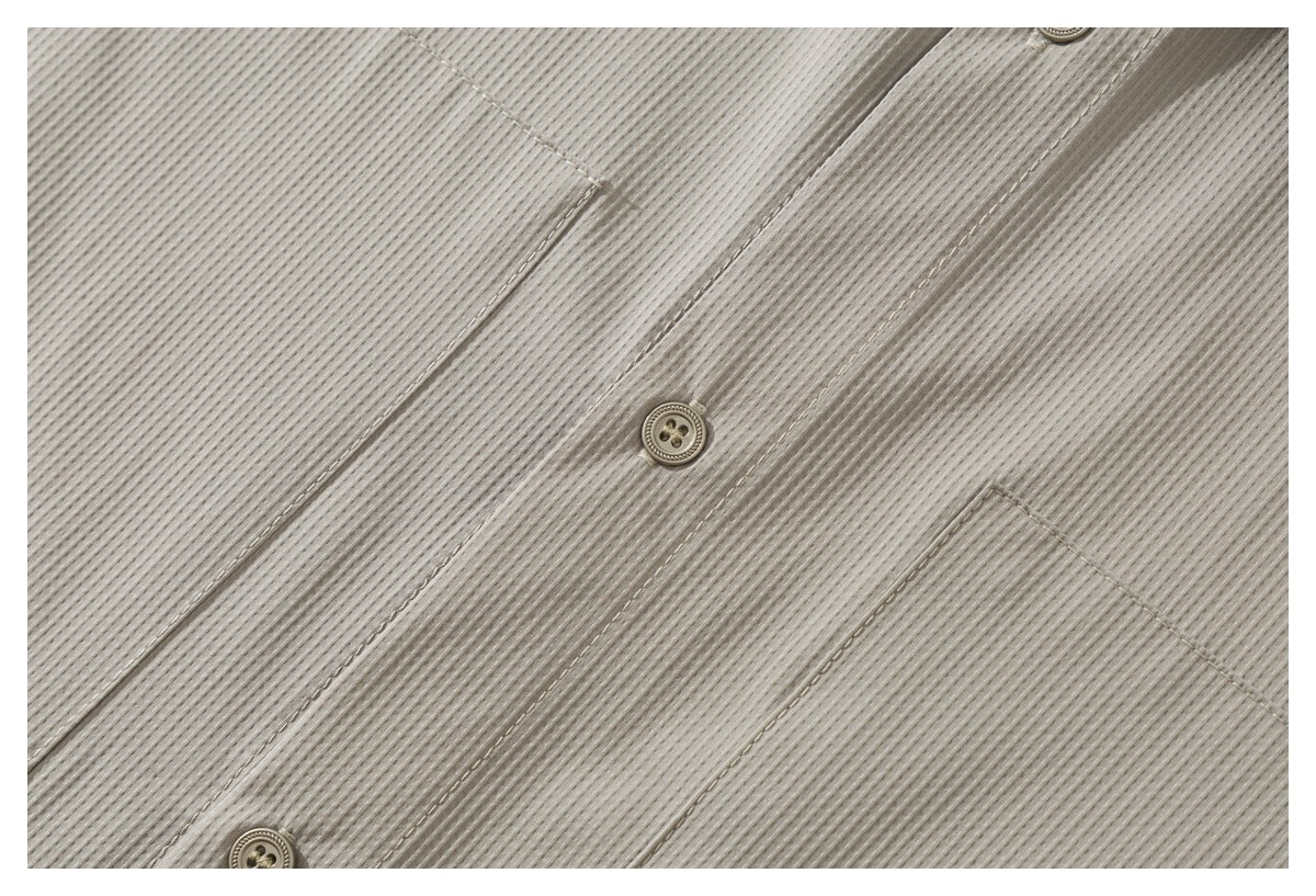 Close-up of the light taupe shirt’s ribbed fabric, button placket, stitching, and edge of a chest pocket.