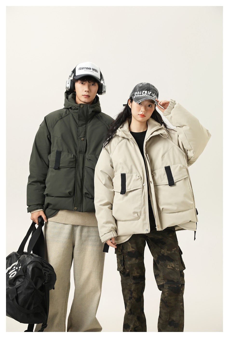 Two models pose in dark olive and light beige hooded utility jackets with oversized flap pockets and black tabs.