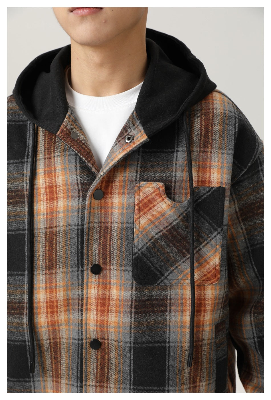 Close view of the plaid hooded shirt jacket showing its black hood, drawstrings, snap buttons, and chest pocket.