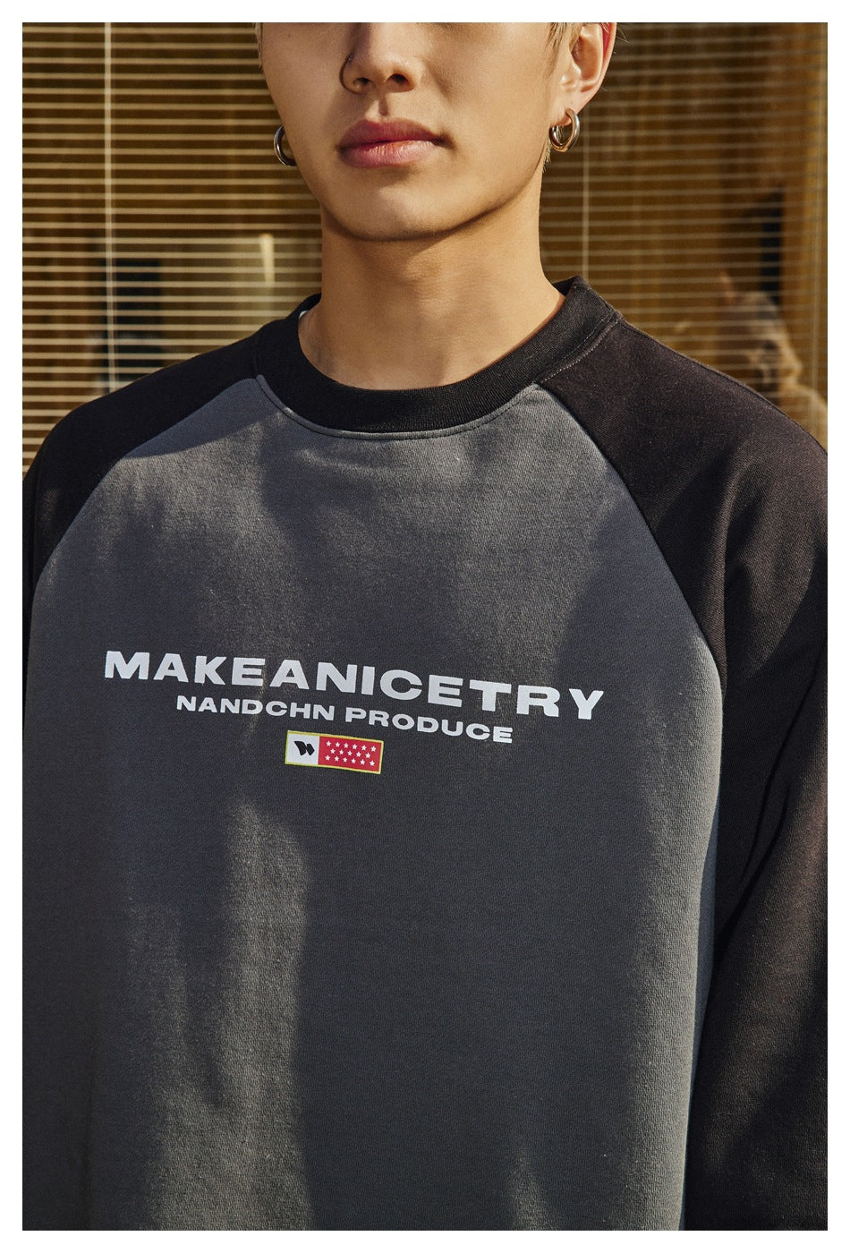 Close view of a model wearing a charcoal raglan sweatshirt with black sleeves and white chest lettering.
