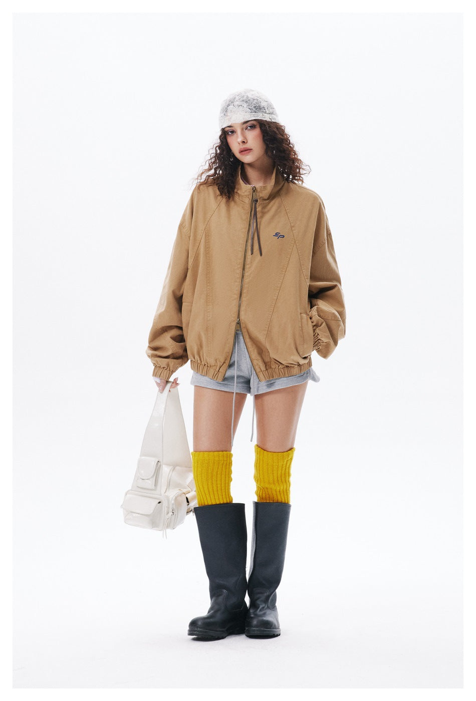 Front view of a model wearing an oversized tan jacket with a full-length zipper, stand collar, and gathered cuffs and hem.
