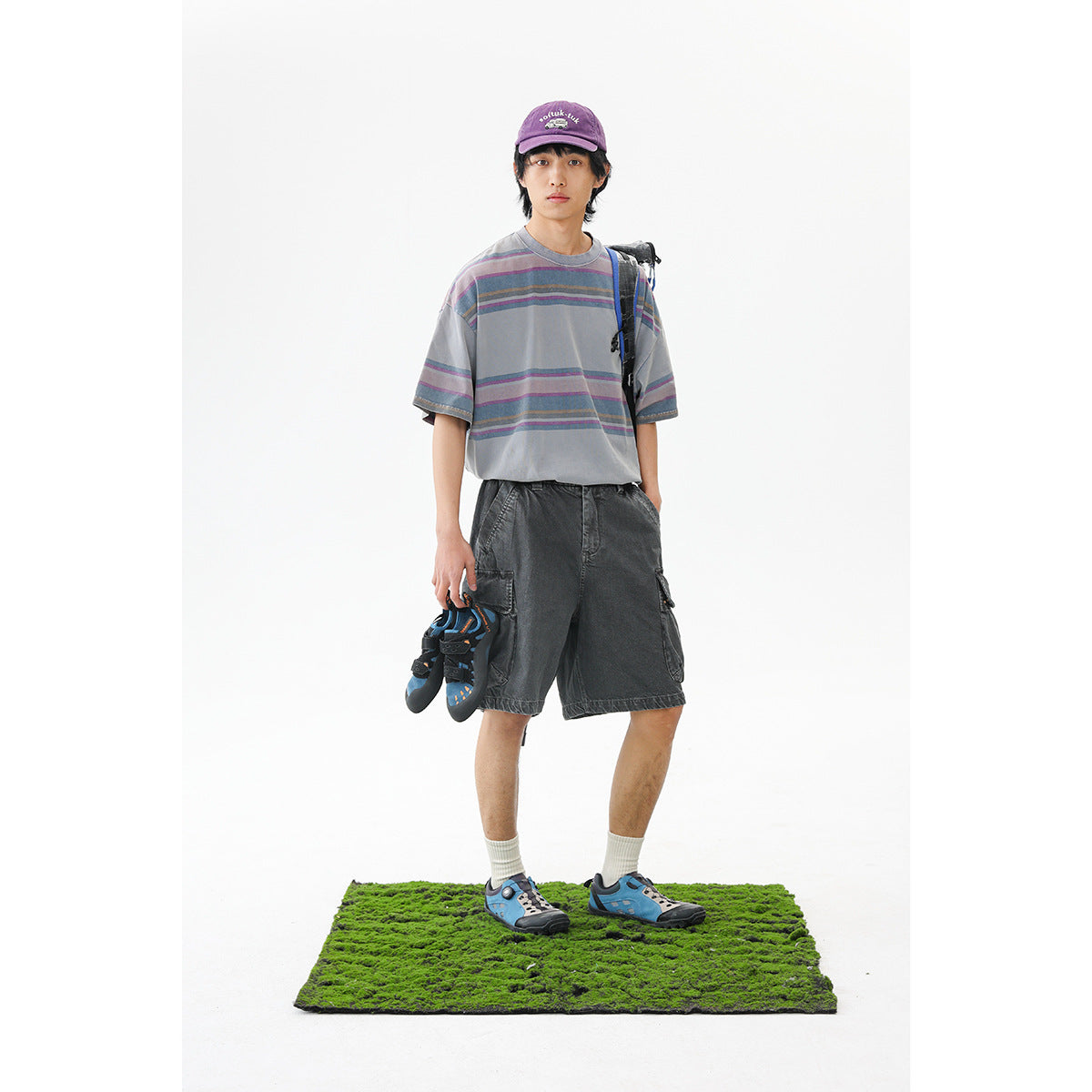 Model wearing an oversized gray T-shirt with muted multicolor stripes and dark gray cargo shorts.