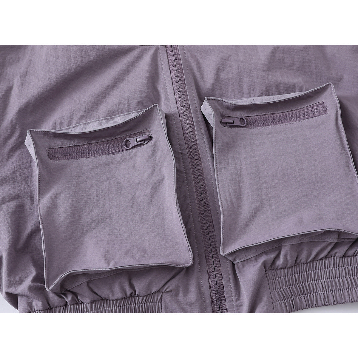 Close-up of two large zippered flap pockets on a muted lavender-gray jacket.