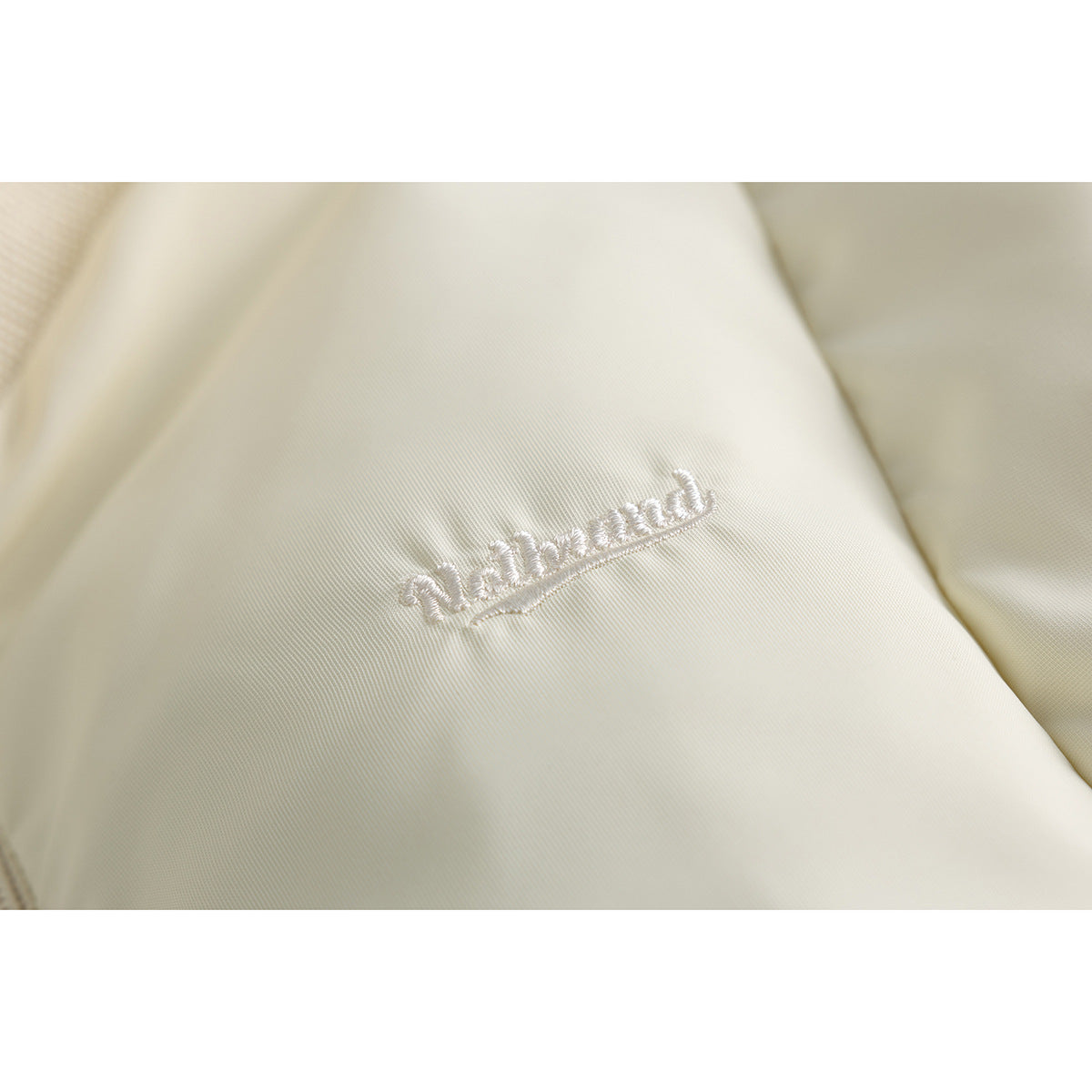 Close-up of white embroidered lettering on the ivory fabric of a jacket.