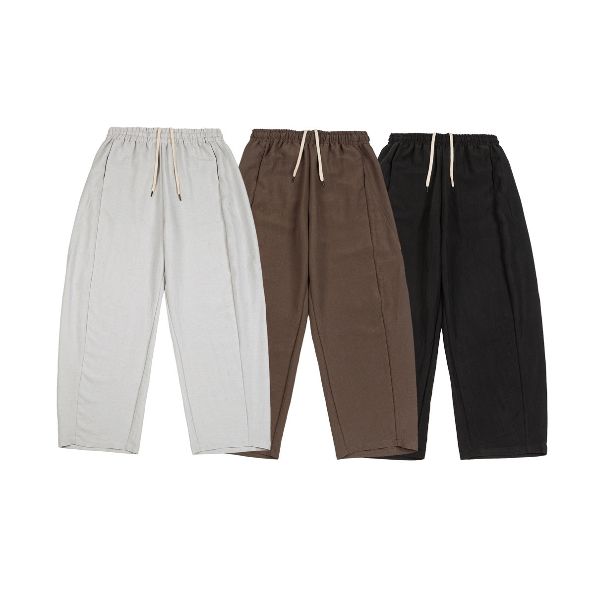 Front view of relaxed trousers in light gray, brown, and black, each with an elastic waist and drawstring.