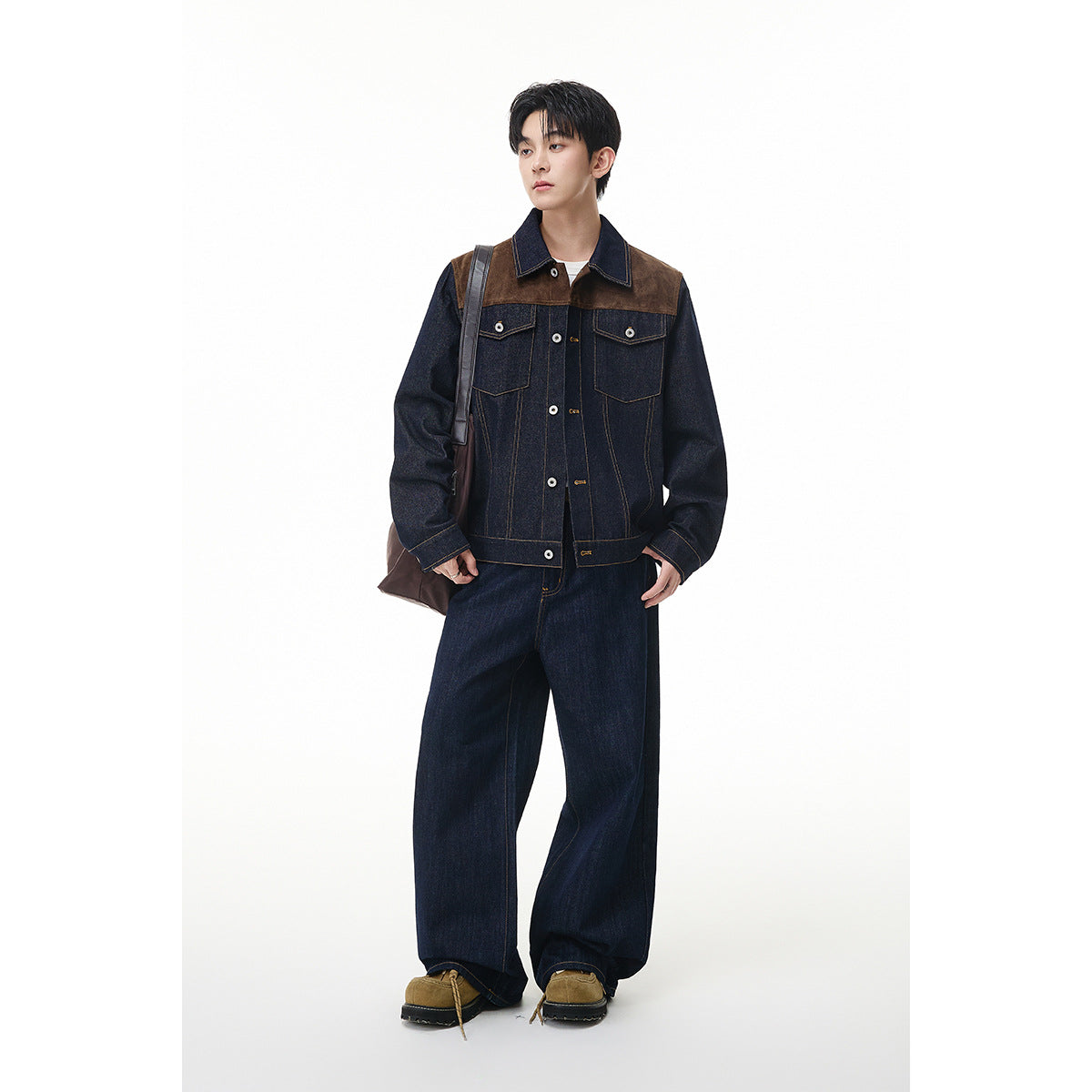 Full-length front view of a model wearing a dark denim jacket with brown shoulder panels and wide-leg jeans.