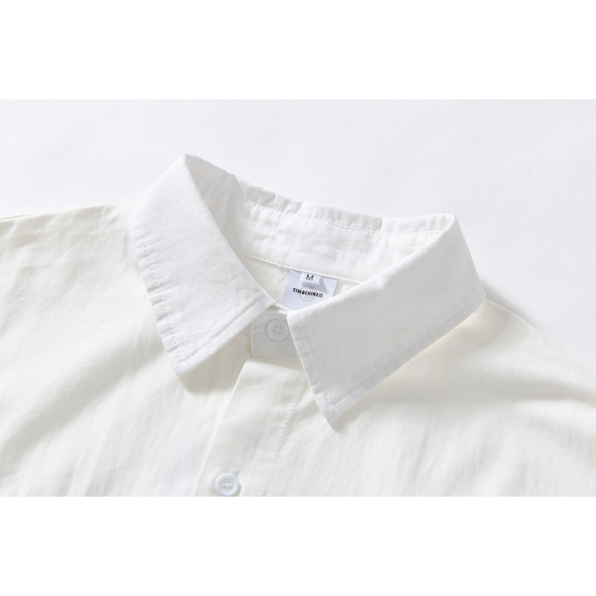 Close-up of a white shirt's pointed collar, top button, and sewn-in neck label.