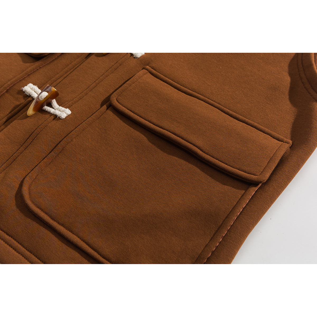 Close-up of a rust-brown vest showing its large flap pocket and braided cord toggle closure.
