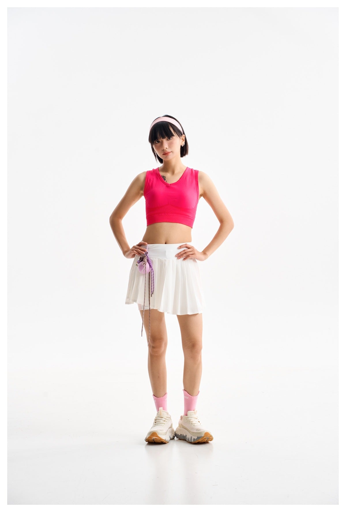 Model wearing a bright pink sleeveless crop top and white pleated tennis skirt with pink socks.