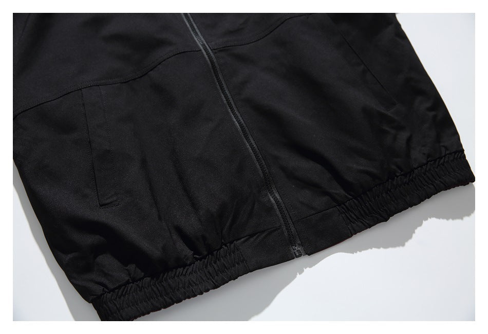 Close-up of the black jacket's lower front, showing the zipper, welt pockets, and elastic hem.