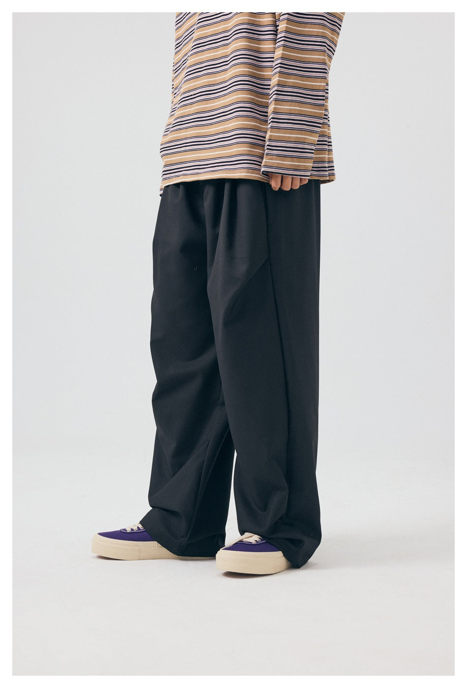Rear three-quarter view of a model wearing black wide-leg trousers and a tan striped shirt.