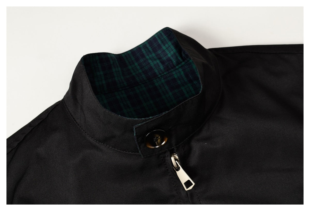 Close-up of a black jacket's stand collar with dark green plaid lining, button tab, and zipper pull.