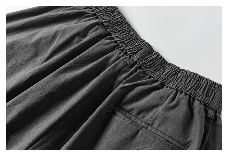 Close-up of dark pants showing a gathered elastic waistband and a slim welt pocket.