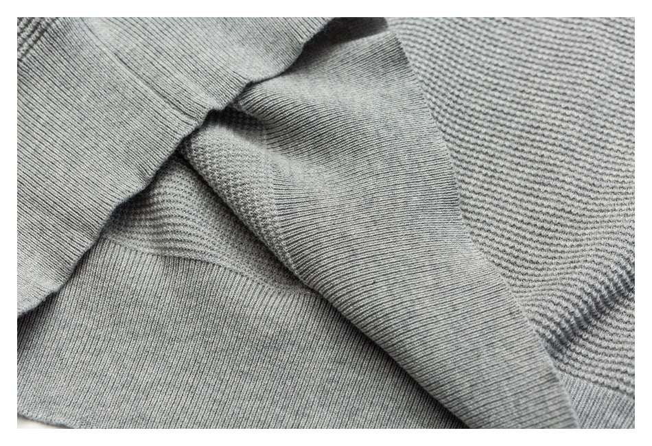 Close-up of the light gray sweater’s ribbed hem and textured knit fabric, folded to show the edge.