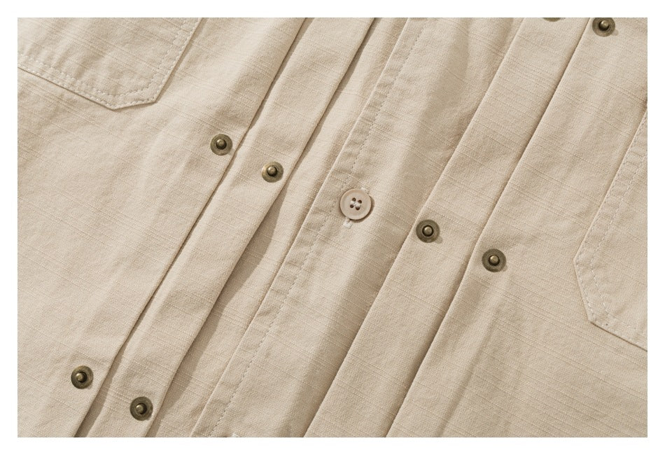 Close-up of a beige shirt showing its button placket, metal snaps, and chest pocket edges.