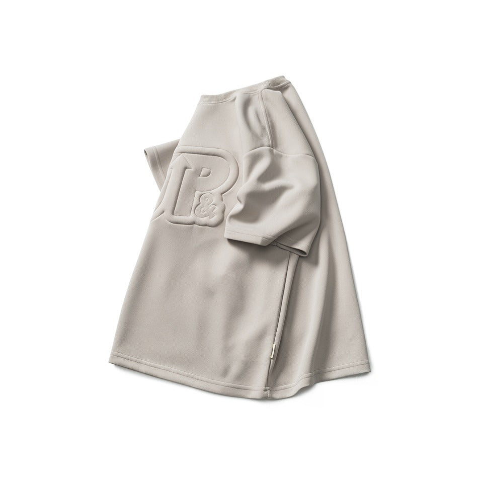Light beige short-sleeve crew-neck T-shirt with a large raised tonal chest logo, displayed against white.