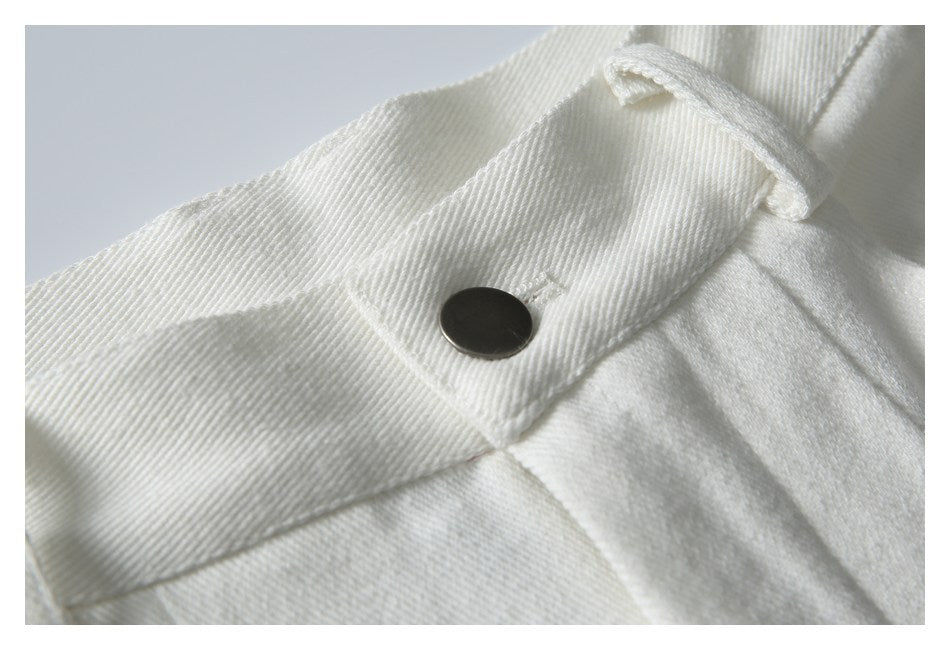 Close-up of white trousers showing a dark waistband button, belt loop, and stitching.