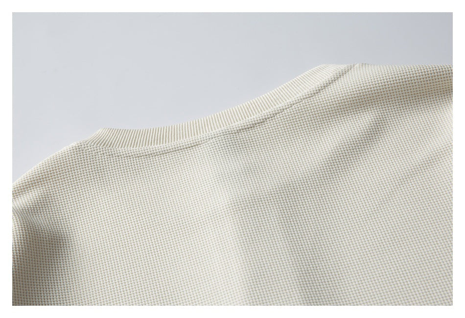 Close-up of the cream waffle-knit garment's ribbed neckline and shoulder seam.