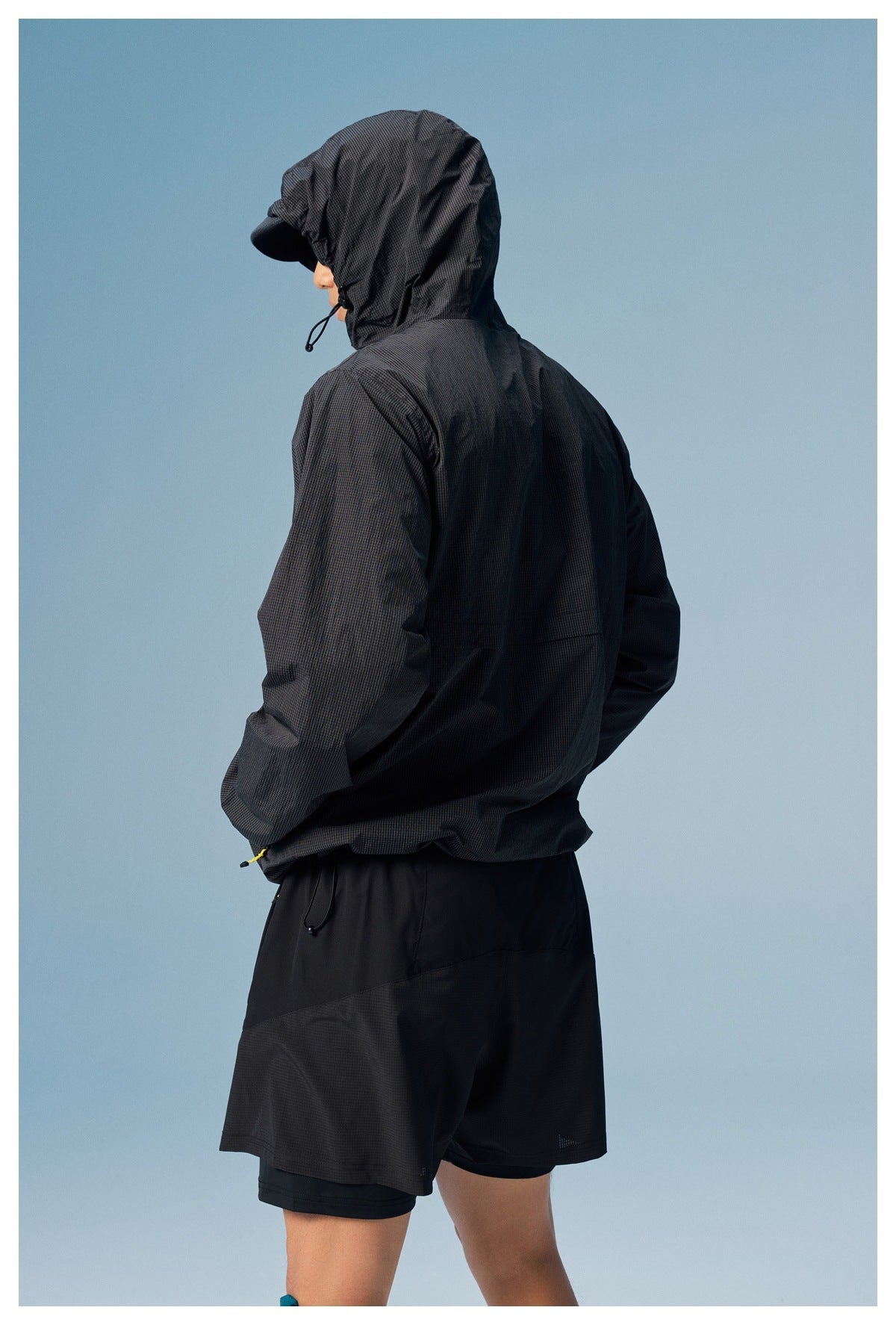 Person wearing a black hooded jacket and black shorts, shown from the side and back.