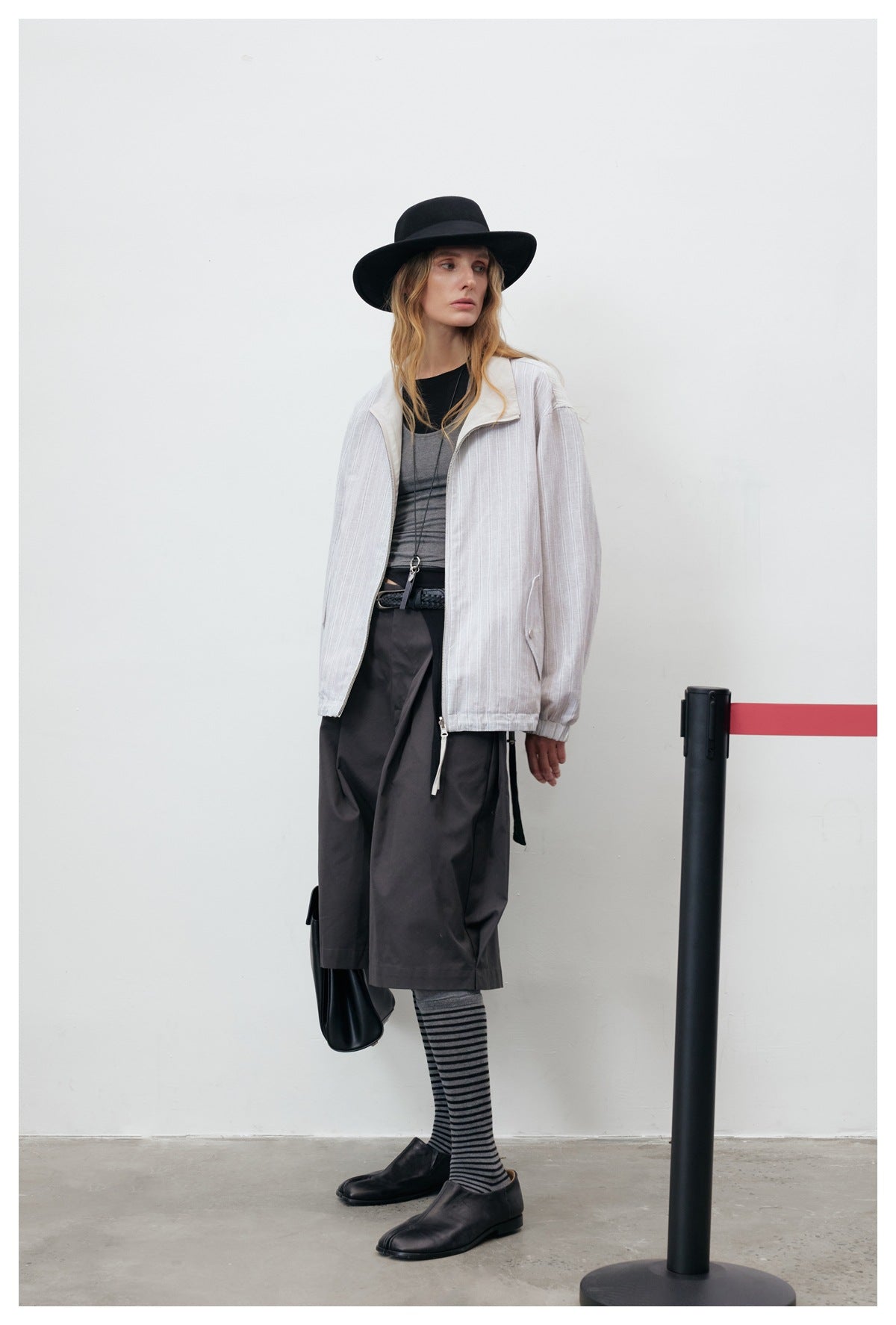 Model wearing an open light gray pinstriped zip jacket with dark wide-leg shorts and striped knee socks.