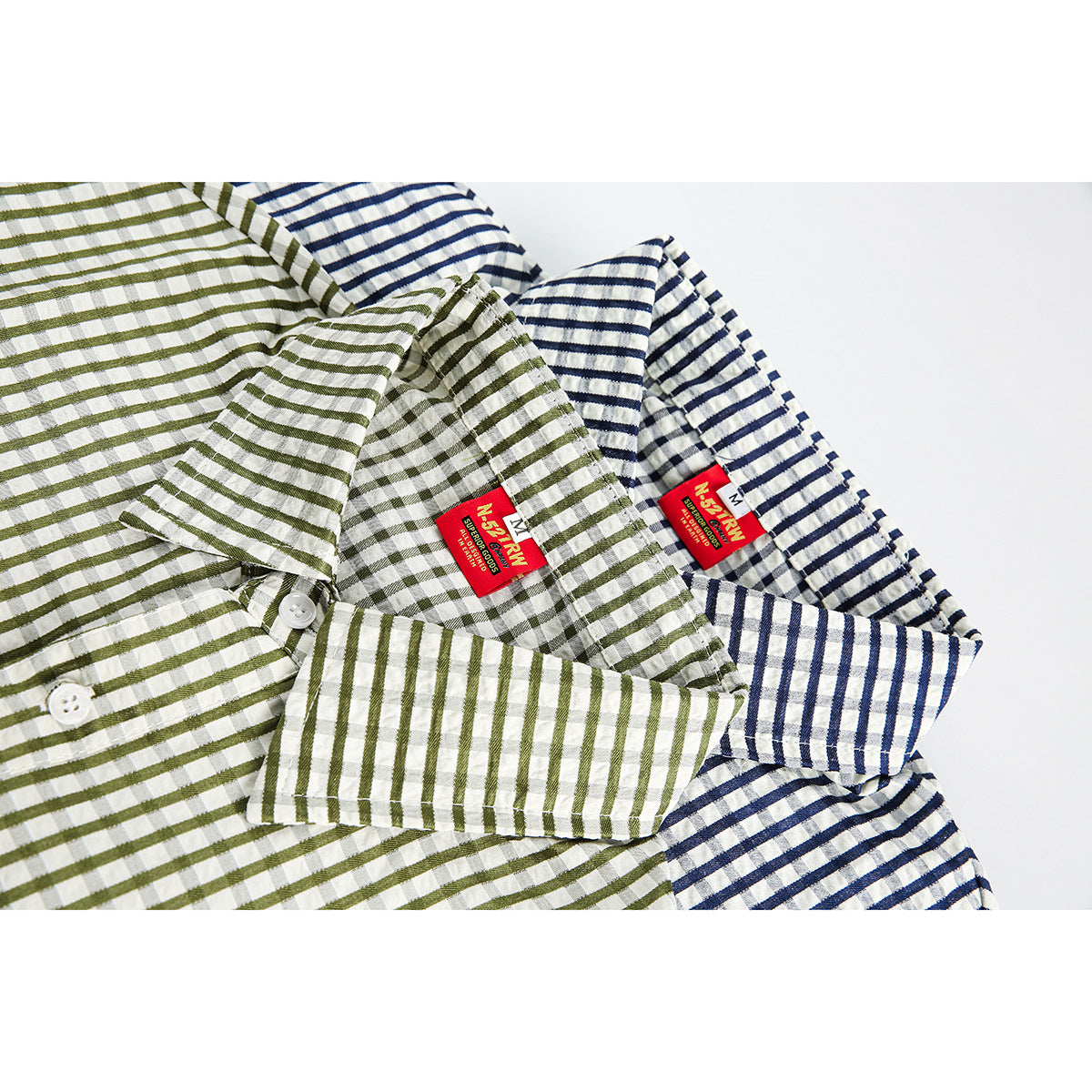 Close-up of olive and navy striped short-sleeve shirts folded together, showing their collars, buttons and labels.