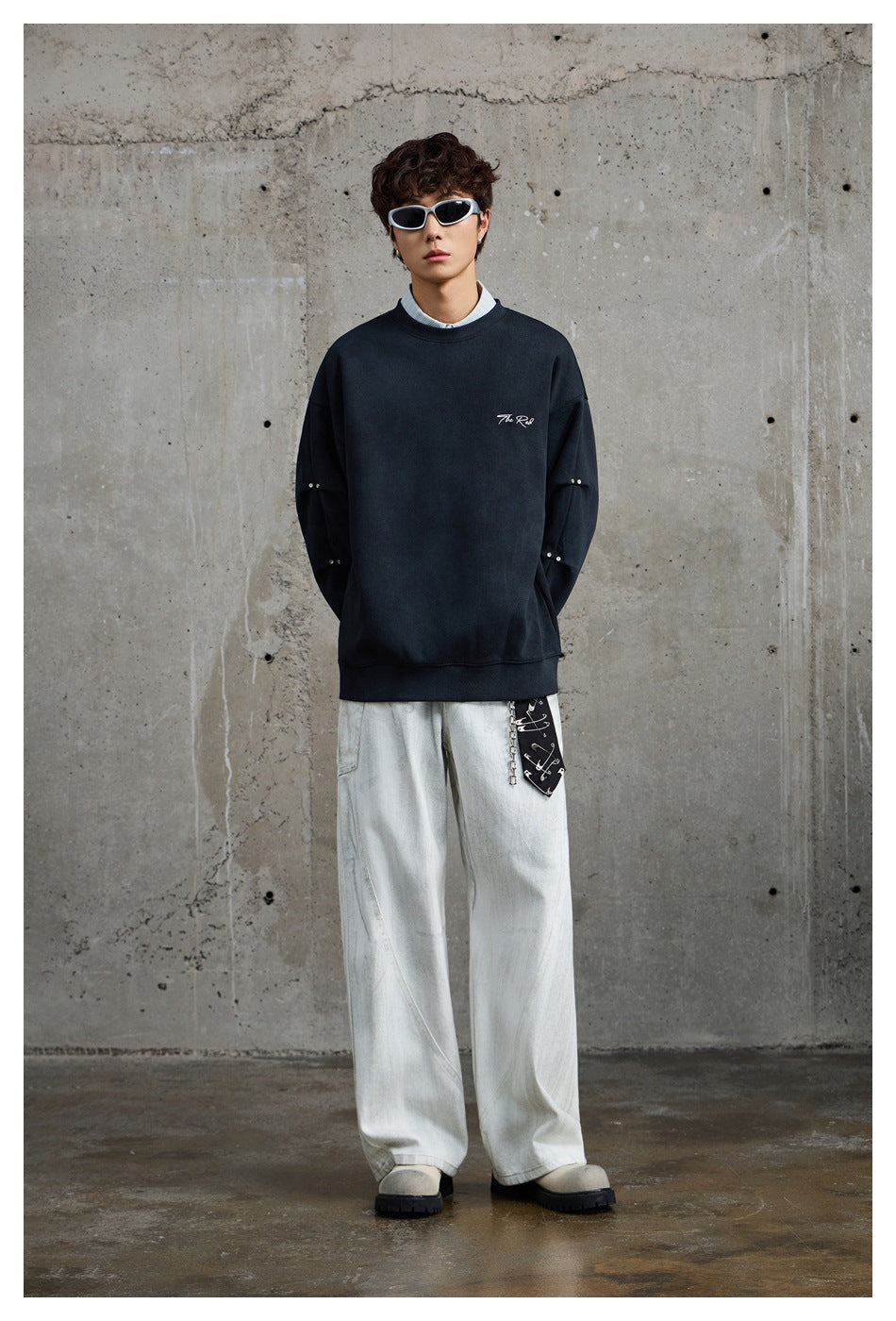 Full-length front view of a model in a dark navy crewneck sweatshirt and loose white trousers.